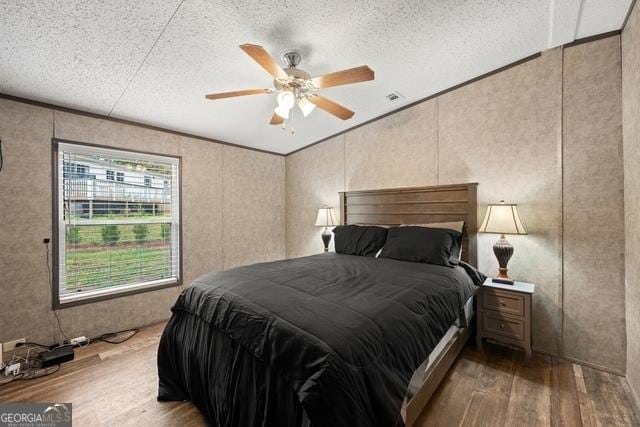 bedroom featuring ceiling fan, a textured ceiling, ornamental molding, and wood finished floors