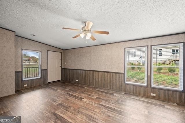 empty room with plenty of natural light, wainscoting, dark wood finished floors, and a textured ceiling