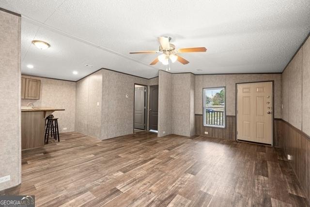 unfurnished living room featuring ceiling fan, a textured ceiling, wainscoting, and wood finished floors