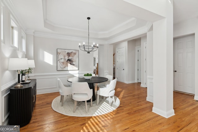 dining room featuring a notable chandelier, ornamental molding, a tray ceiling, and light wood-type flooring