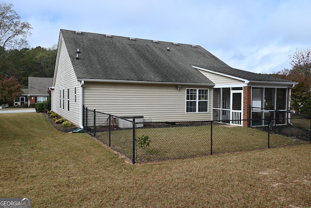 rear view of property featuring a sunroom, a shingled roof, fence, and a lawn