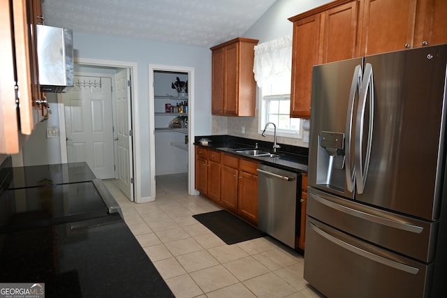 kitchen featuring stainless steel appliances, dark countertops, a sink, brown cabinetry, and light tile patterned floors