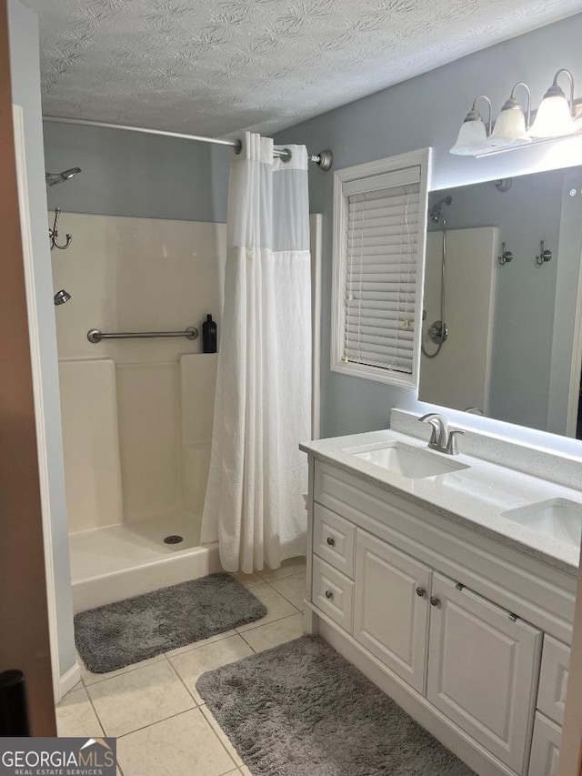 bathroom with a textured ceiling, a shower stall, tile patterned floors, a sink, and double vanity