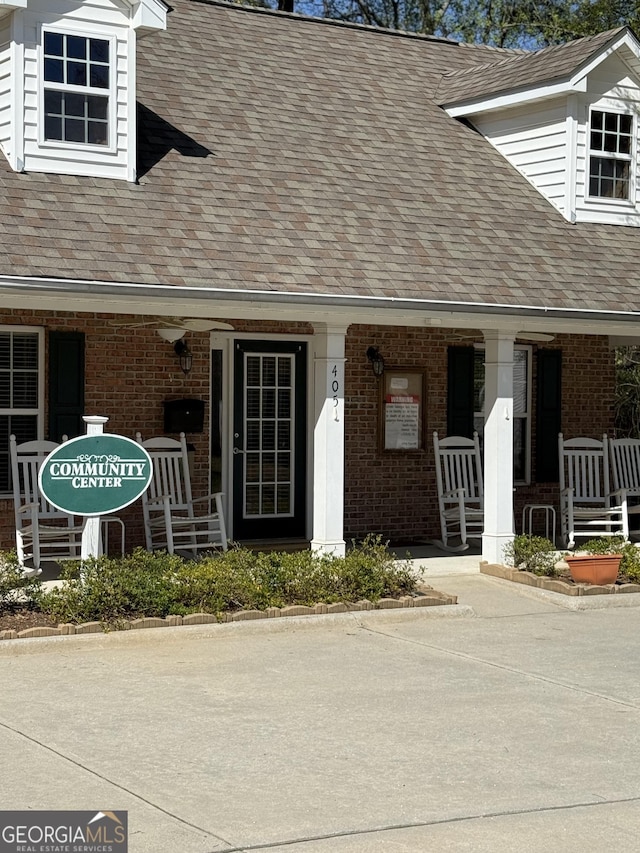 doorway to property with covered porch, brick siding, and roof with shingles