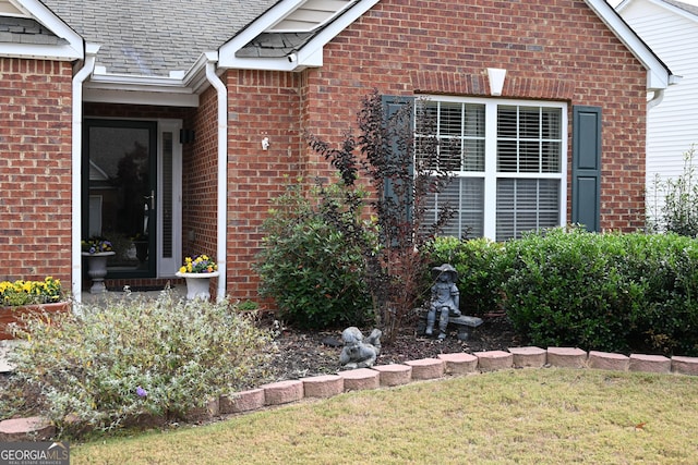 entrance to property featuring brick siding and a shingled roof