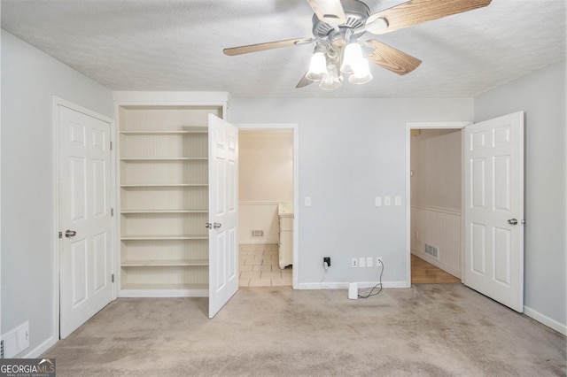 unfurnished bedroom with ceiling fan, light colored carpet, ensuite bath, and a textured ceiling