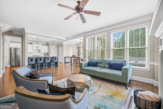 living area with light wood-style flooring, recessed lighting, ceiling fan with notable chandelier, baseboards, and ornamental molding