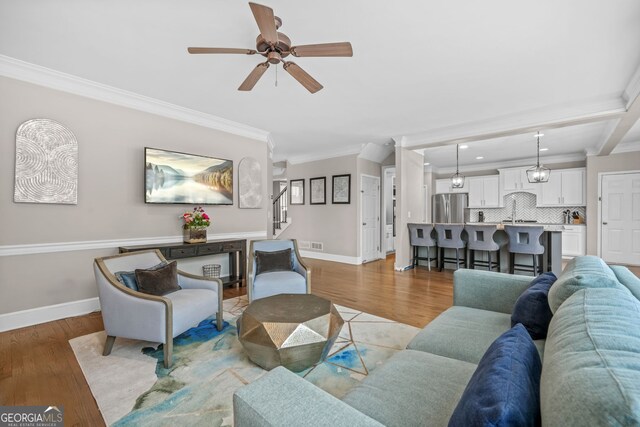 living room with visible vents, baseboards, stairs, light wood-type flooring, and crown molding