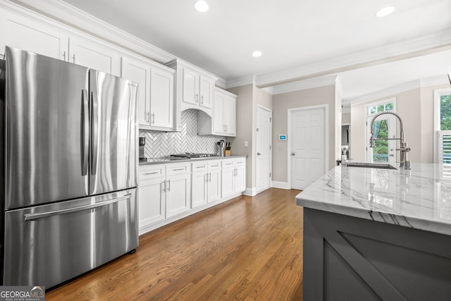 kitchen with white cabinets, appliances with stainless steel finishes, backsplash, crown molding, and a sink