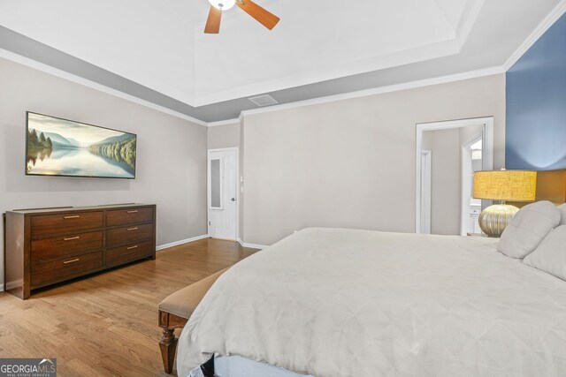 bedroom with baseboards, ornamental molding, a raised ceiling, and wood finished floors