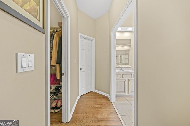 hall with baseboards, a sink, and light wood finished floors