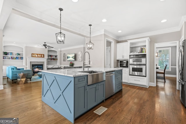 kitchen featuring a glass covered fireplace, light stone countertops, stainless steel appliances, white cabinetry, and a sink