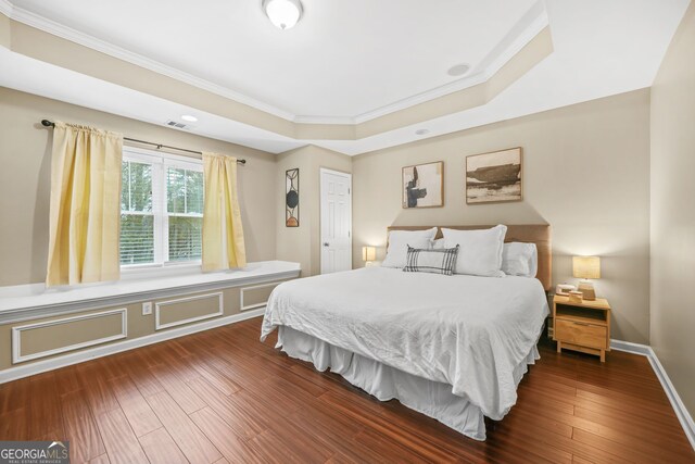 bedroom with baseboards, crown molding, a tray ceiling, and dark wood-style flooring