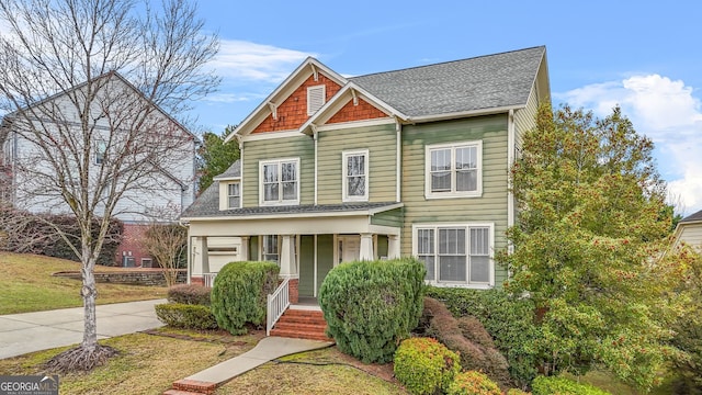 view of front of house featuring covered porch, driveway, a shingled roof, and a front lawn