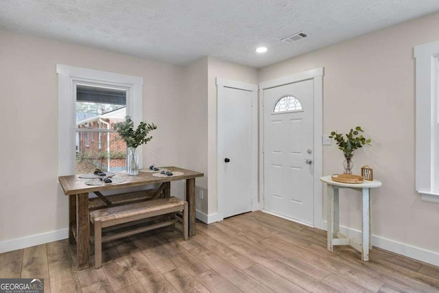 foyer entrance with plenty of natural light, a textured ceiling, and light wood-type flooring