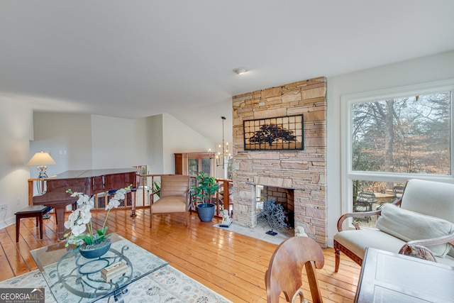 living room with a stone fireplace, hardwood / wood-style floors, and an inviting chandelier