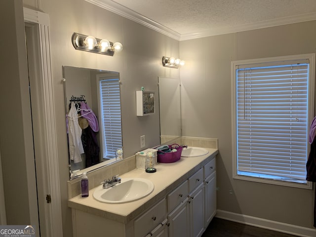 bathroom with a textured ceiling, a sink, baseboards, double vanity, and crown molding