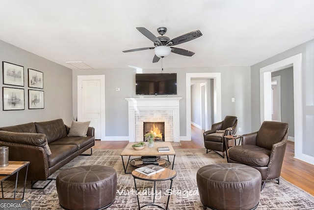 living room with wood-type flooring, a tile fireplace, and ceiling fan