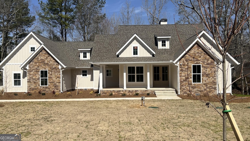 view of front facade featuring stone siding, french doors, roof with shingles, board and batten siding, and a chimney