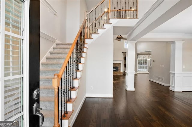 foyer entrance with crown molding, dark wood finished floors, decorative columns, a high ceiling, and a stone fireplace