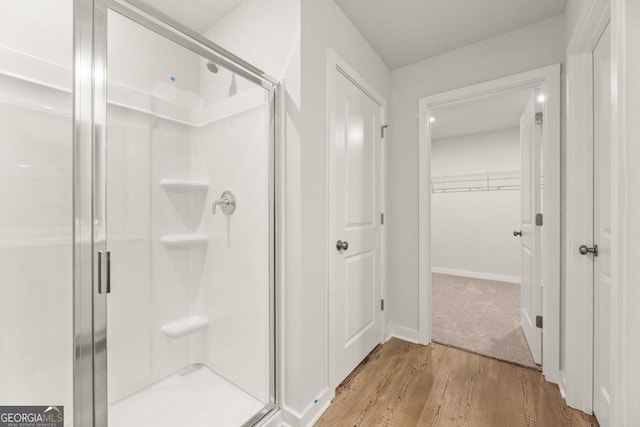 full bathroom with a shower stall, baseboards, a walk in closet, and wood finished floors