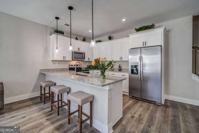 kitchen featuring white cabinets, appliances with stainless steel finishes, a kitchen breakfast bar, wood finished floors, and a peninsula