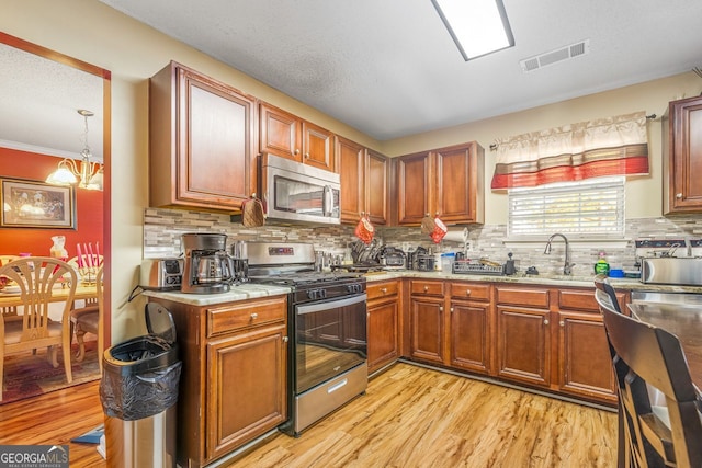 kitchen with a chandelier, light wood-type flooring, appliances with stainless steel finishes, pendant lighting, and backsplash