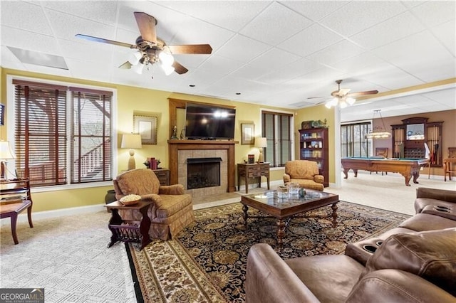 carpeted living room with a ceiling fan, a paneled ceiling, a tiled fireplace, and baseboards