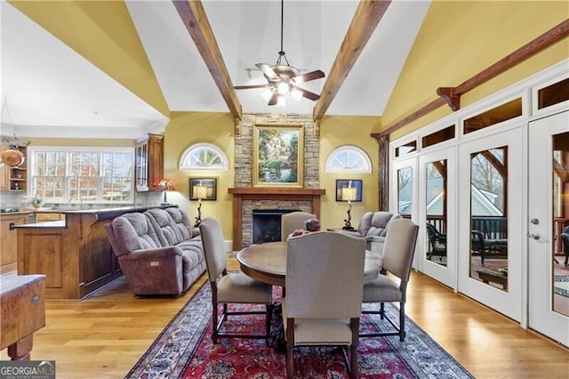 dining room with a fireplace, ceiling fan, light wood-type flooring, and lofted ceiling with beams