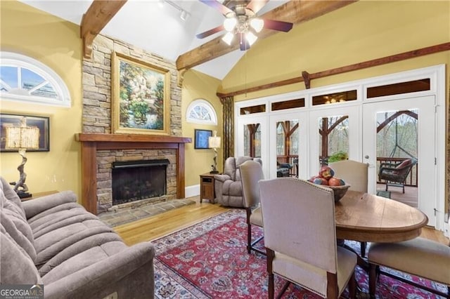 dining room with a large fireplace, lofted ceiling with beams, ceiling fan, and light wood-style flooring