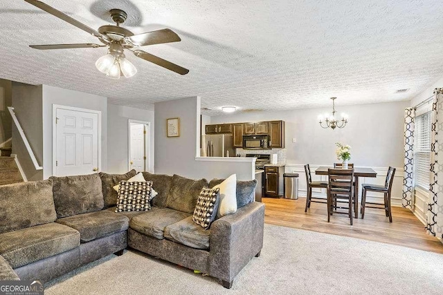 living room featuring ceiling fan with notable chandelier, light hardwood / wood-style flooring, and a textured ceiling