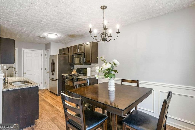 dining space featuring an inviting chandelier, sink, light hardwood / wood-style floors, and a textured ceiling