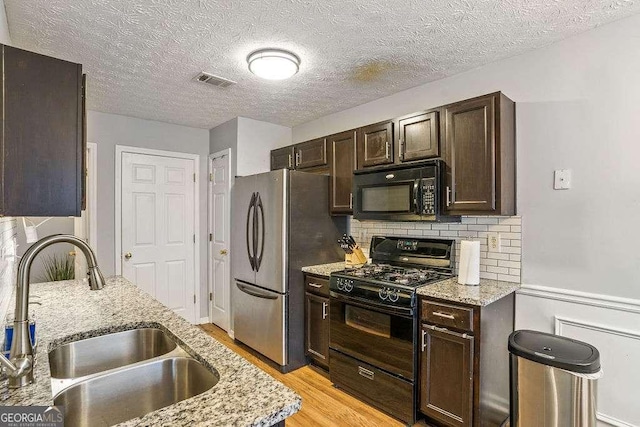 kitchen featuring sink, dark brown cabinets, black appliances, light stone countertops, and light wood-type flooring