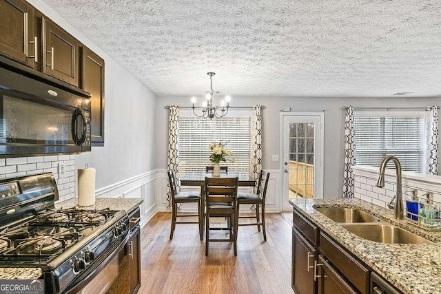 kitchen with sink, dark brown cabinets, dark hardwood / wood-style flooring, light stone countertops, and black appliances