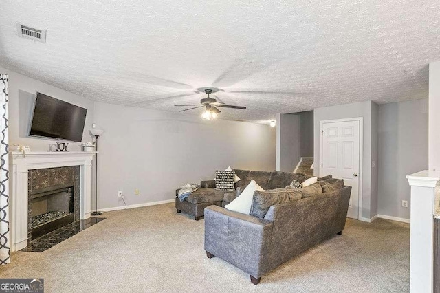 living room with ceiling fan, light colored carpet, a fireplace, and a textured ceiling