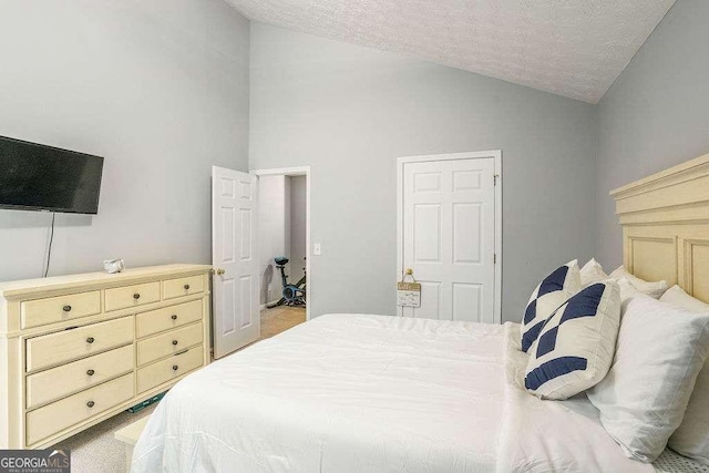 bedroom with vaulted ceiling, light colored carpet, and a textured ceiling