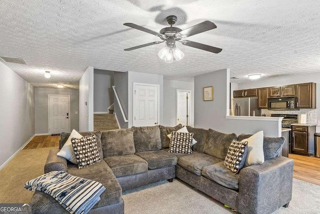 living room featuring ceiling fan, light hardwood / wood-style floors, and a textured ceiling