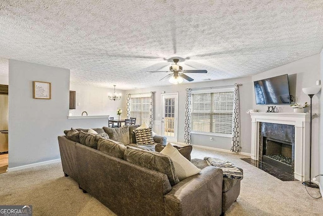 carpeted living room with a premium fireplace, ceiling fan with notable chandelier, and a textured ceiling