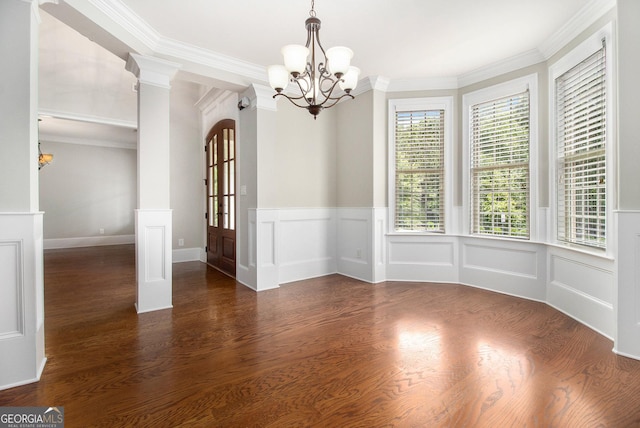 unfurnished dining area with a chandelier, wood finished floors, wainscoting, ornamental molding, and ornate columns