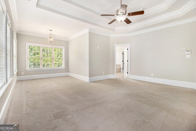 empty room featuring a raised ceiling, crown molding, light carpet, baseboards, and ceiling fan