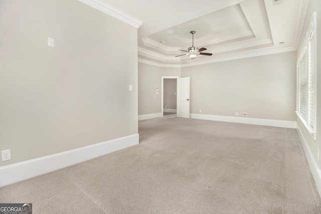 spare room with a tray ceiling, light colored carpet, ceiling fan, crown molding, and baseboards
