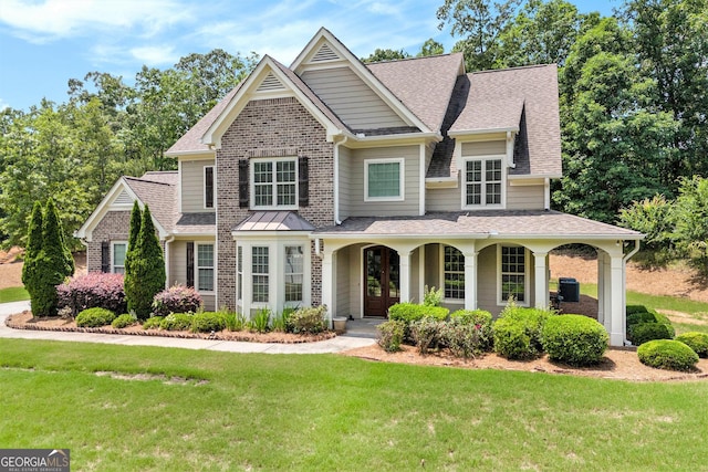 view of front of home with a shingled roof, a front lawn, brick siding, and covered porch