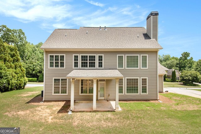 back of house with a patio, a chimney, a yard, and a shingled roof