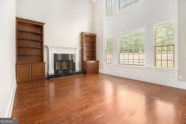 unfurnished living room with wood finished floors, a towering ceiling, a fireplace, and healthy amount of natural light