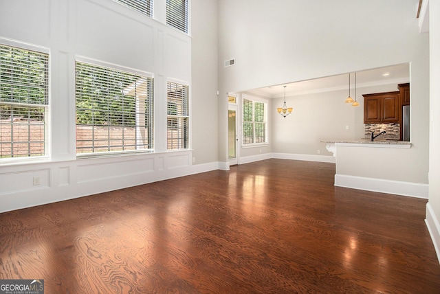 unfurnished living room with a chandelier, dark wood finished floors, a towering ceiling, and ornamental molding