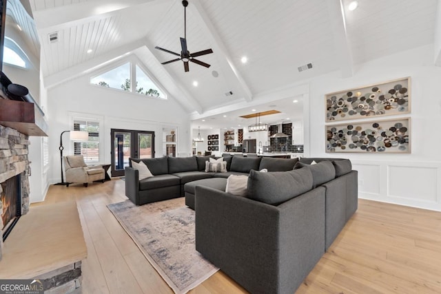 living room with french doors, a stone fireplace, high vaulted ceiling, beam ceiling, and light hardwood / wood-style floors