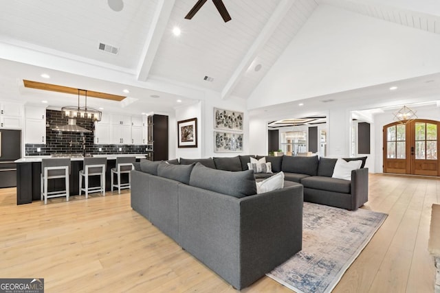 living room featuring french doors, a chandelier, high vaulted ceiling, light hardwood / wood-style flooring, and beam ceiling