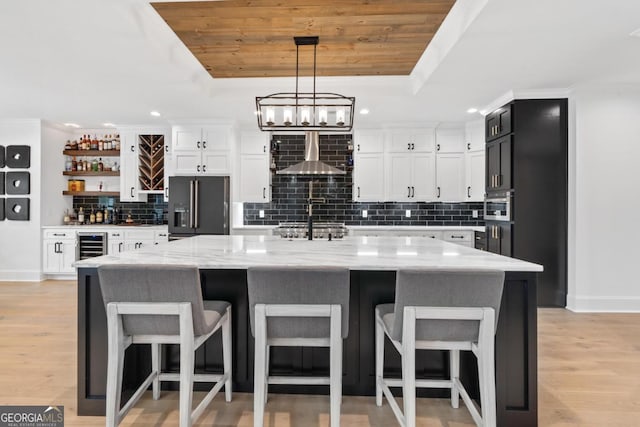 kitchen featuring high quality fridge, decorative light fixtures, a large island with sink, light stone counters, and a tray ceiling