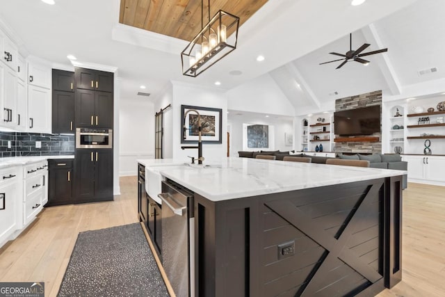 kitchen with pendant lighting, vaulted ceiling with beams, stainless steel appliances, a center island with sink, and light wood-type flooring