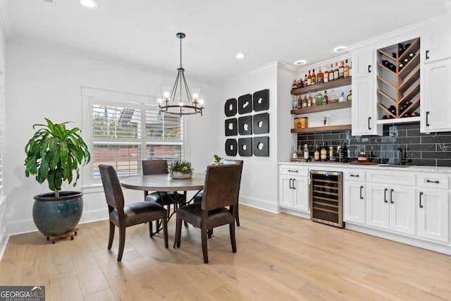 dining area with indoor bar, wine cooler, a notable chandelier, crown molding, and light hardwood / wood-style flooring